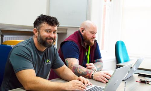 Image of 2 male employees sitting at a desk while using their laptops. Image of 2 male employees sitting at a desk while using their laptops.