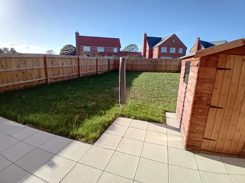 Back garden of St James Place East Bergholt showing a green lawn, patio and shed.